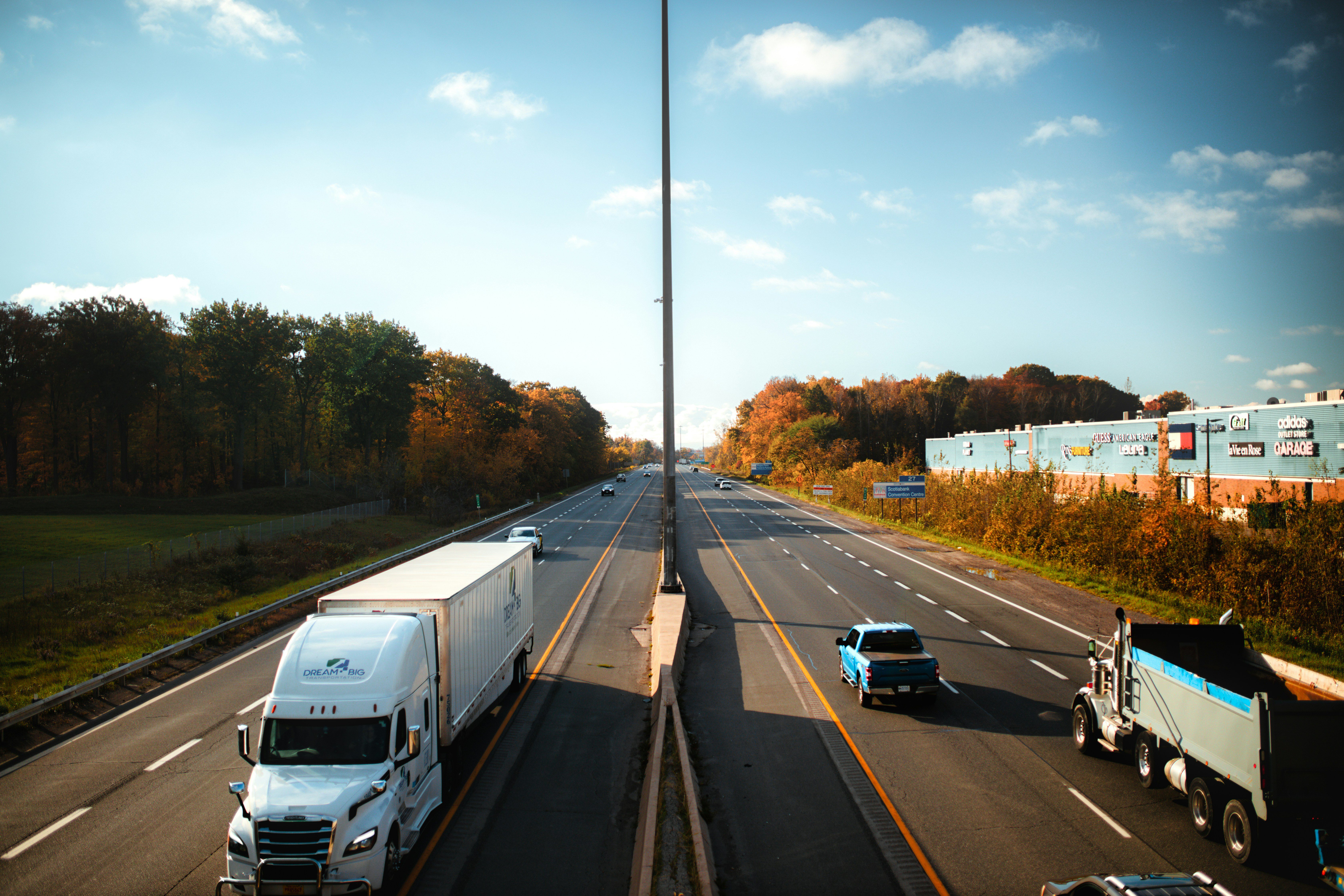 A highway with a couple of trucks and a car on it, surrounded by trees with autumn color leaves